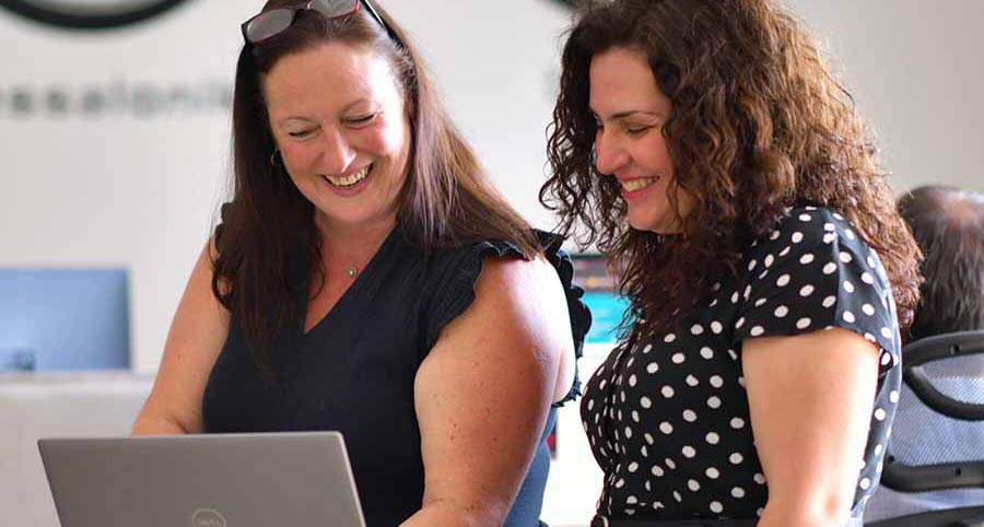 two women smiling at a laptop in an office